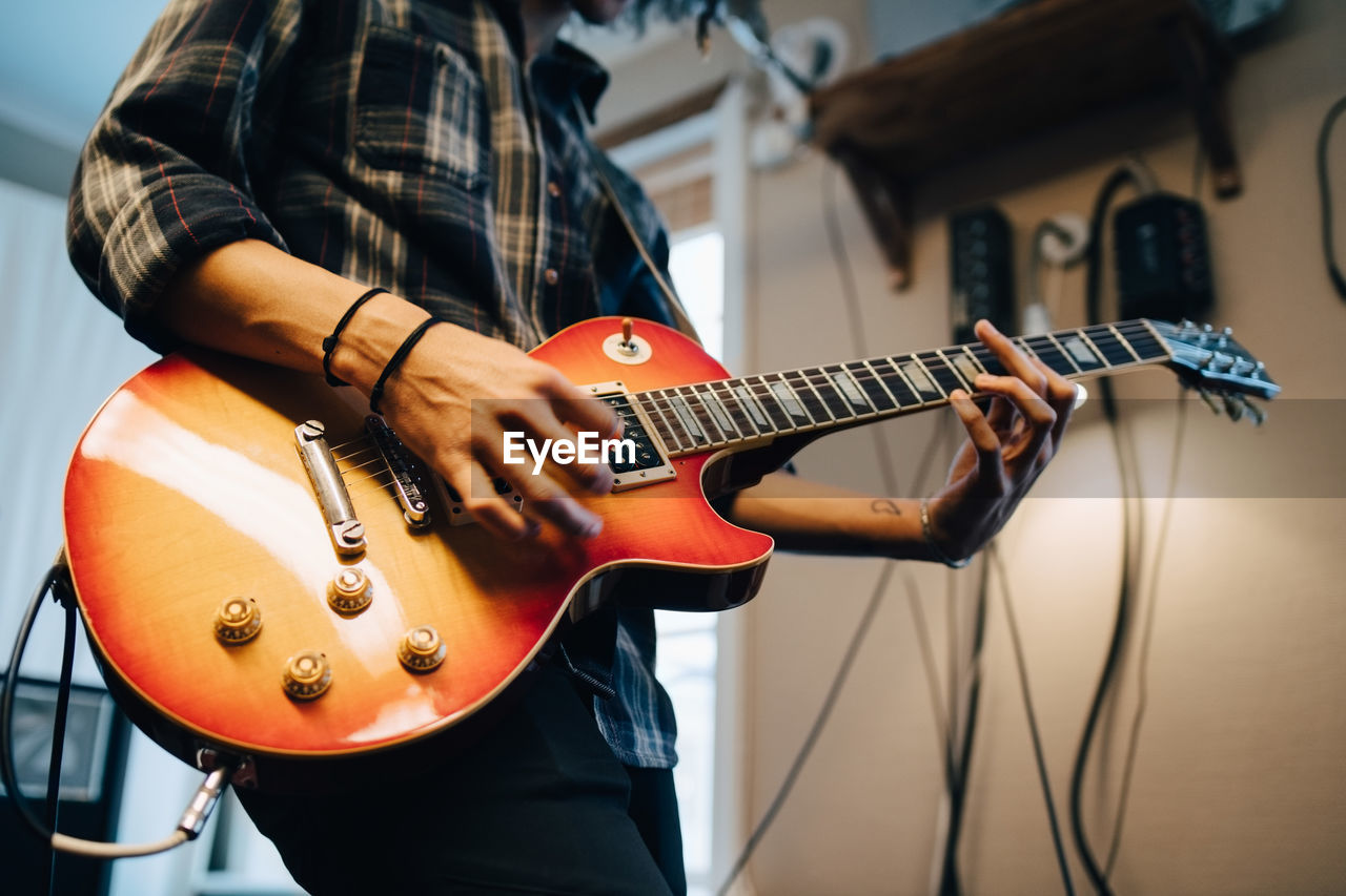 Midsection of man playing guitar while practicing in recording studio