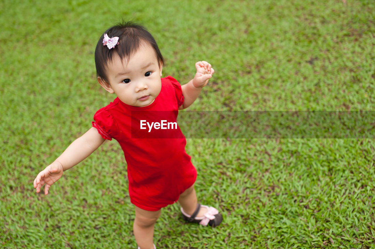 High angle portrait of baby girl standing on grassy field at park