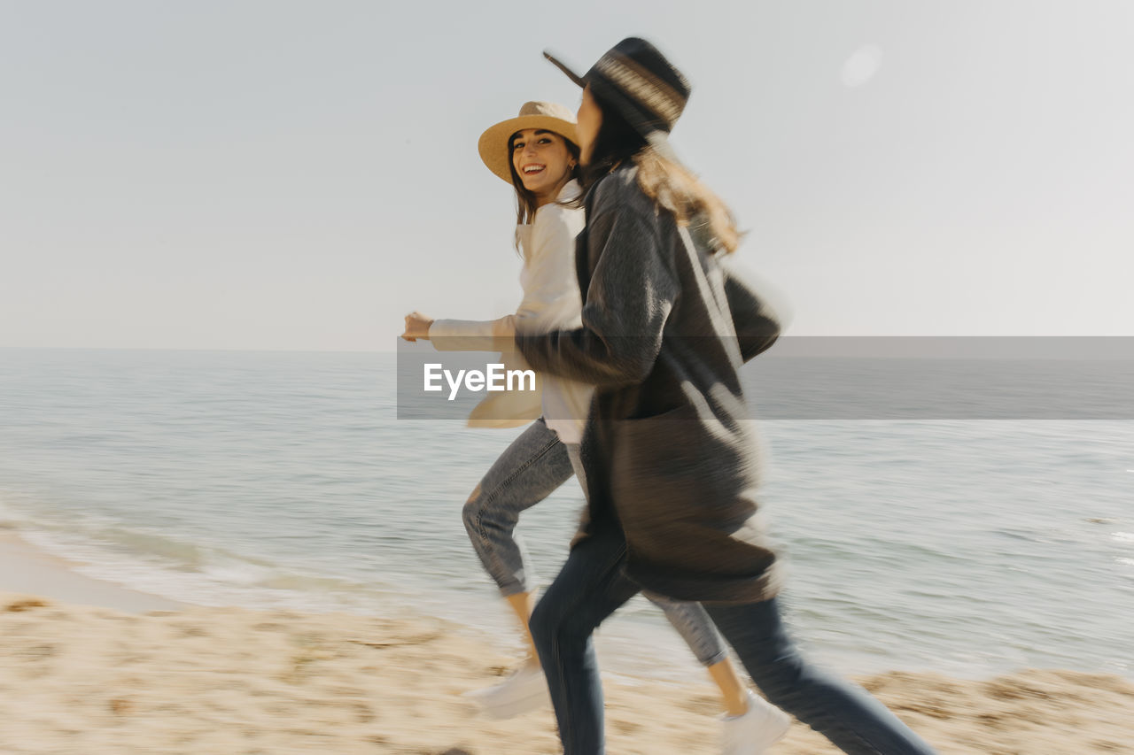 Happy female siblings running at beach on sunny day