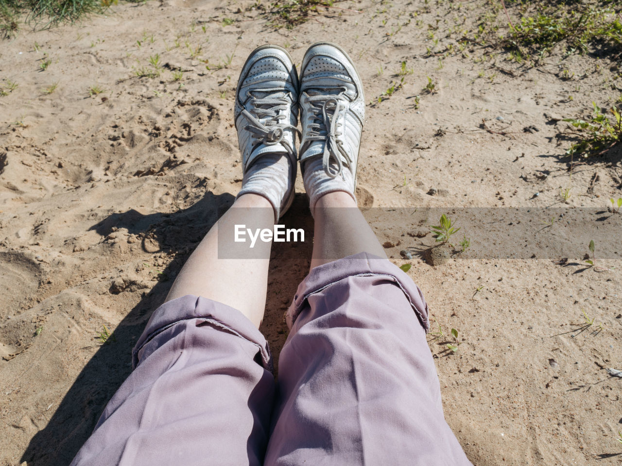 Woman's legs wearing pink pants and white sneakers laying at the beach