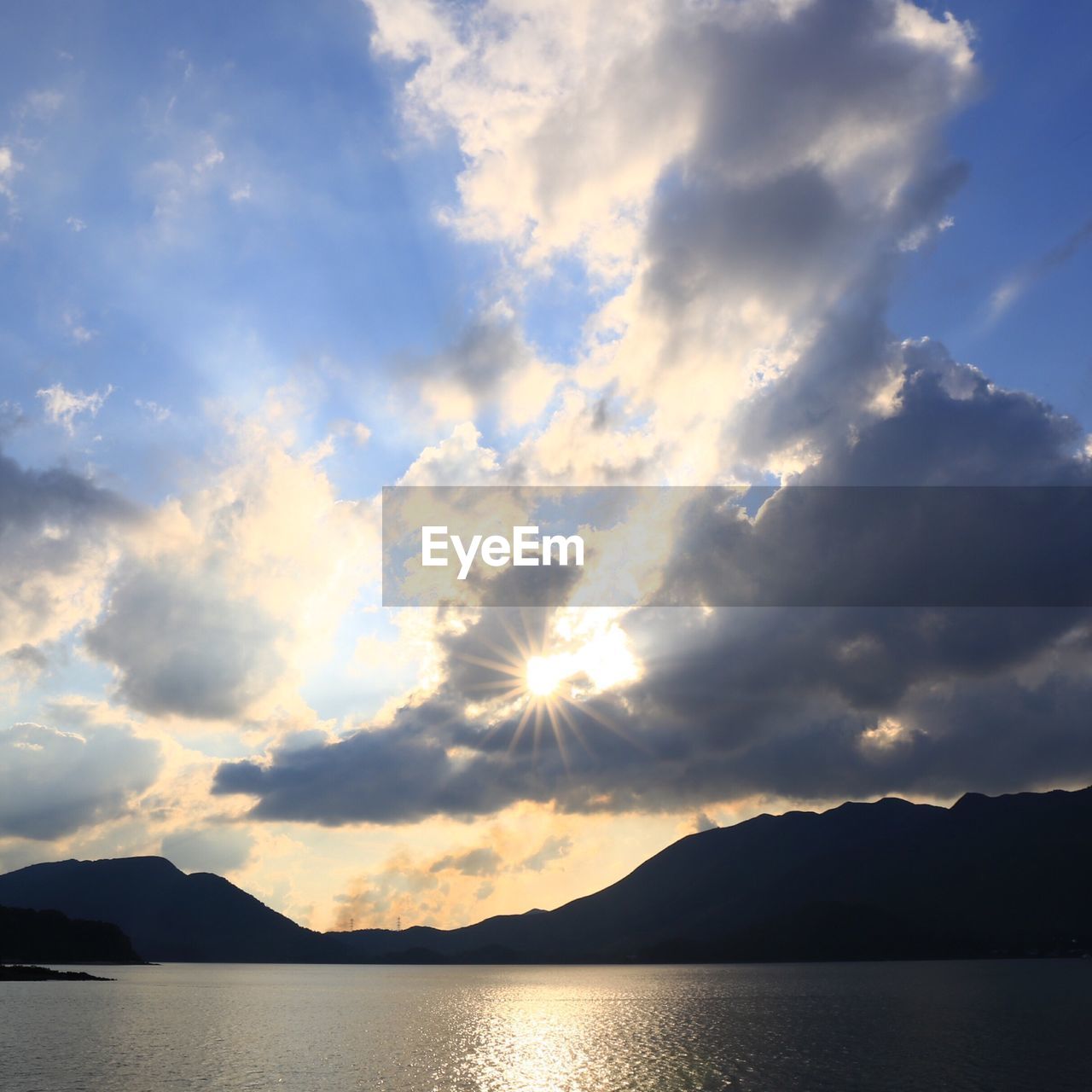 Scenic view of lake and mountains against cloudy sky during sunset
