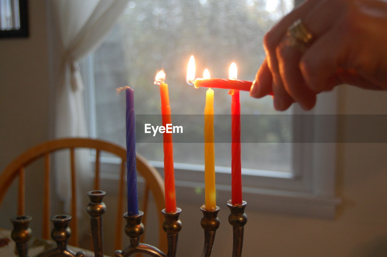 Cropped image of woman igniting candles on hanukkah at home