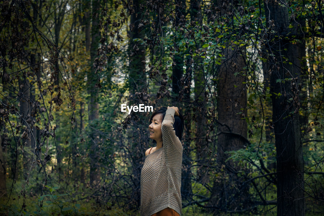 Woman standing by tree trunk in forest