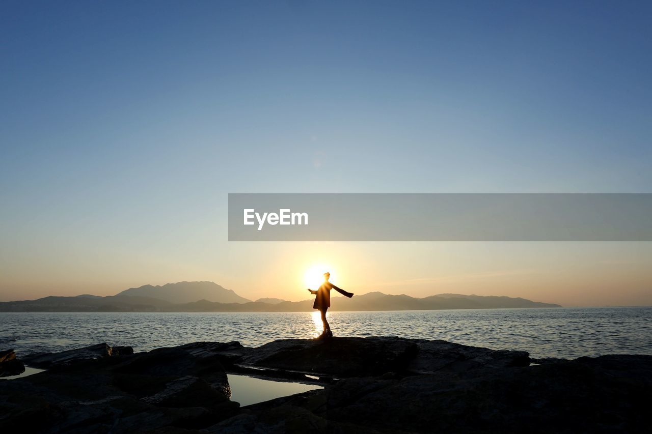 Silhouette person standing at beach against sky during sunset