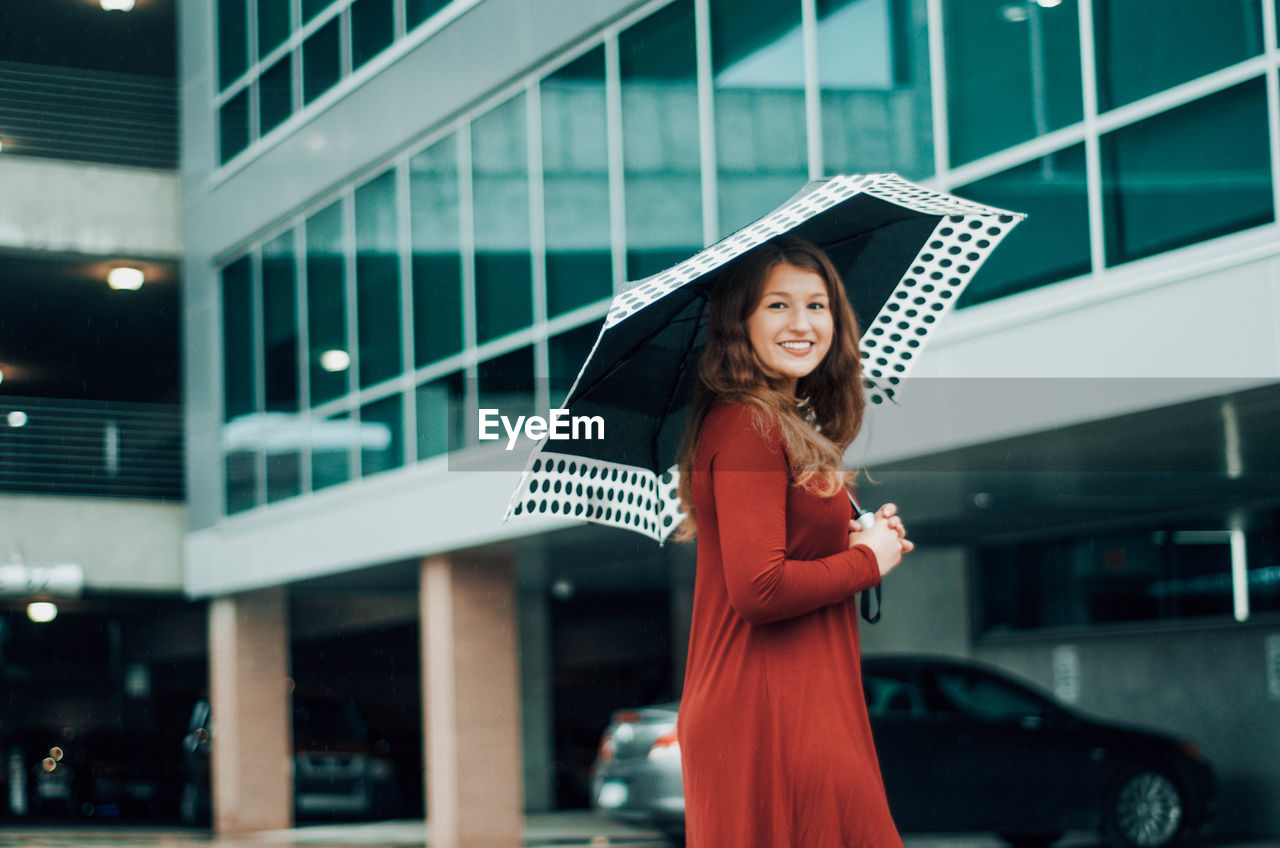 Portrait of smiling girl standing with umbrella in parking lot