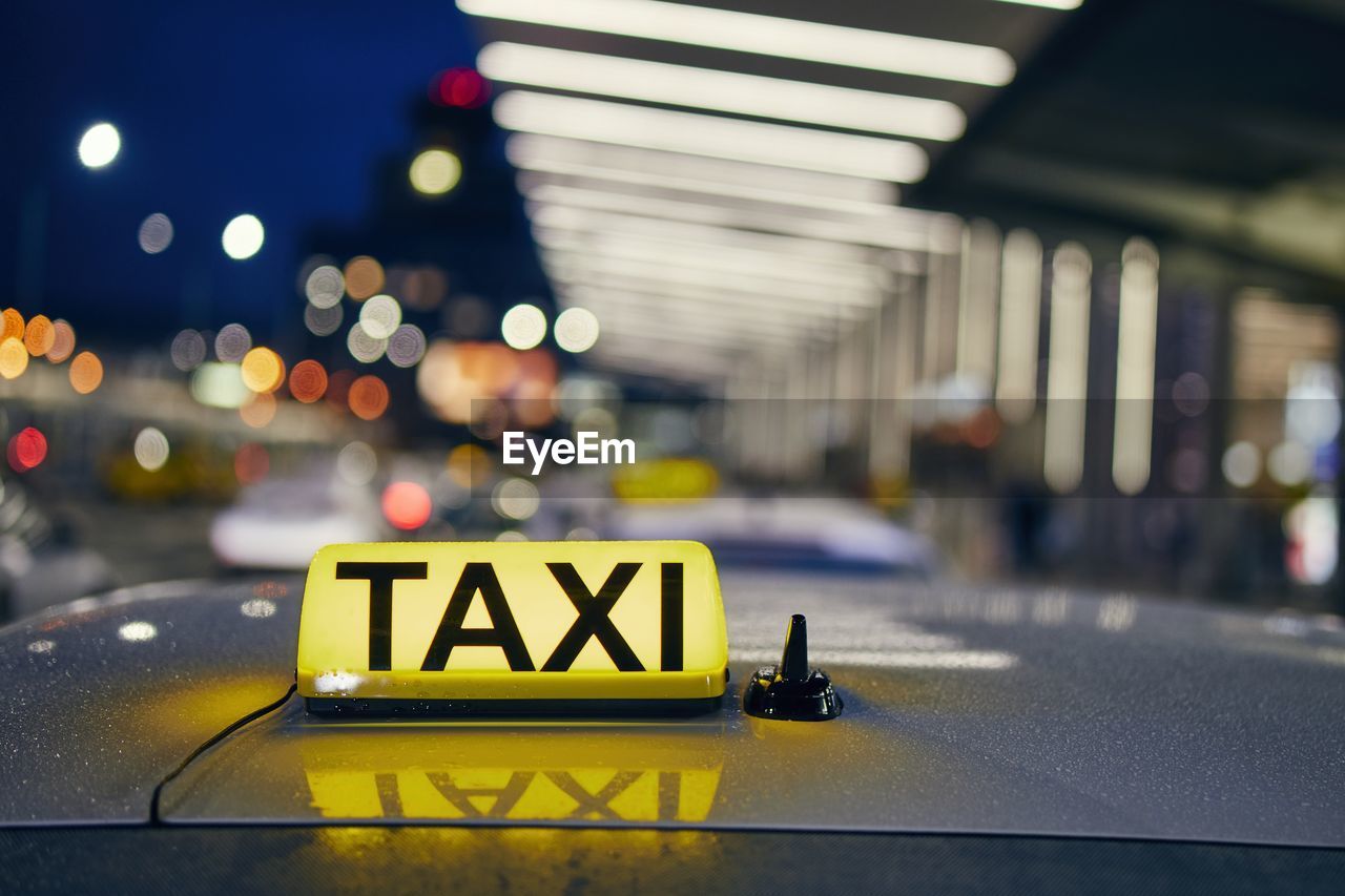 Lighting taxi sign on the roof of car against airport terminal at night.