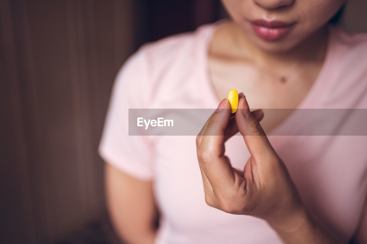 Crop unrecognizable healthy female showing bright yellow vitamin pill during health care routine at home