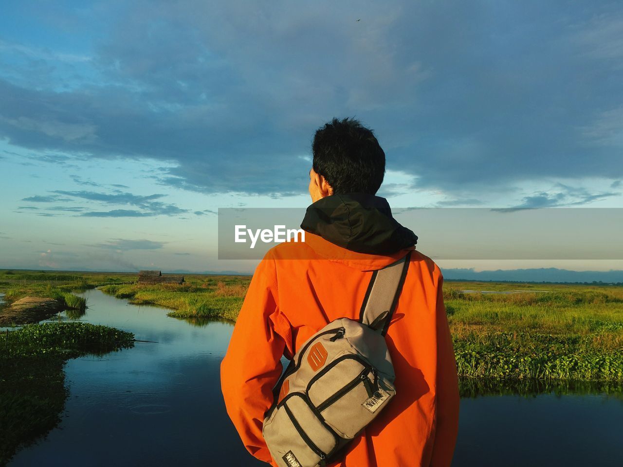 Rear view of man with bag looking at view against cloudy sky