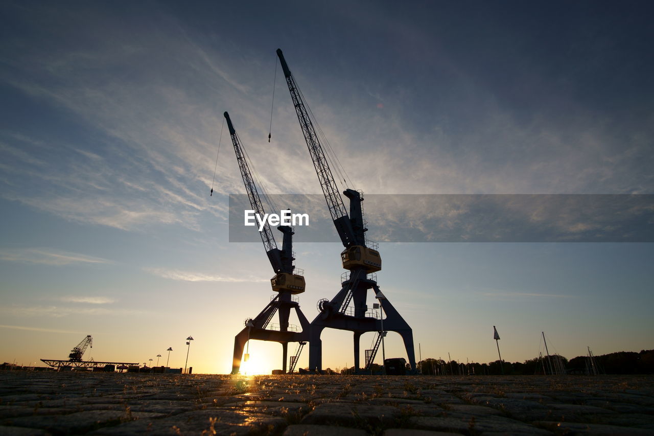Low angle view of silhouette cranes on field against sky at sunset