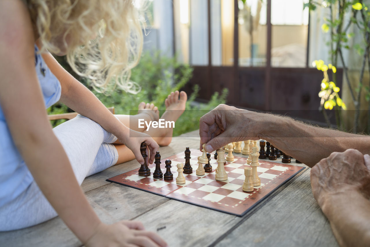 Hands of grandfather playing chess with granddaughter on table