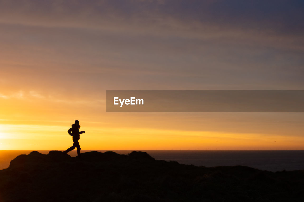 Silhouette of woman walking above ocean at dawn