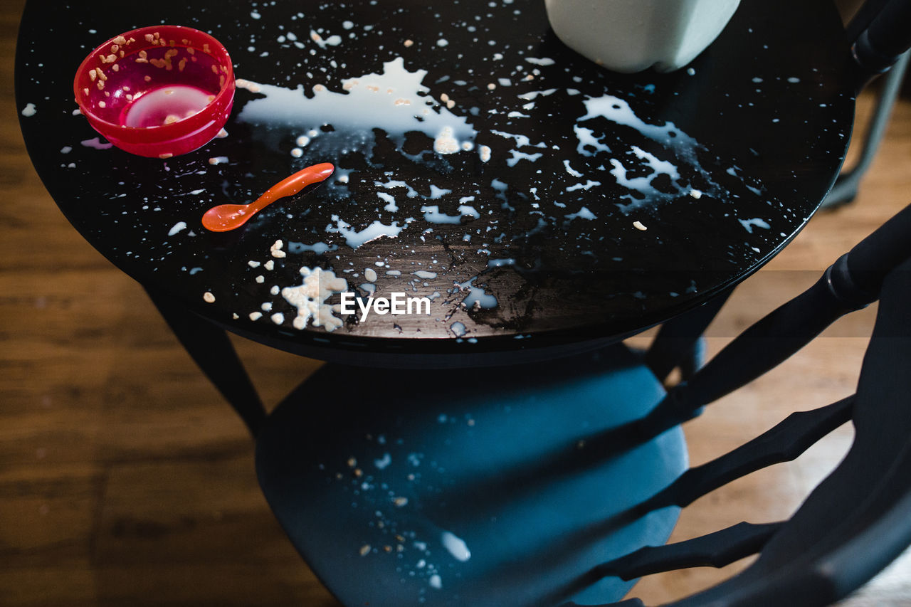 Big mess of spilled milk and cereal on table with empty bowl and spoon