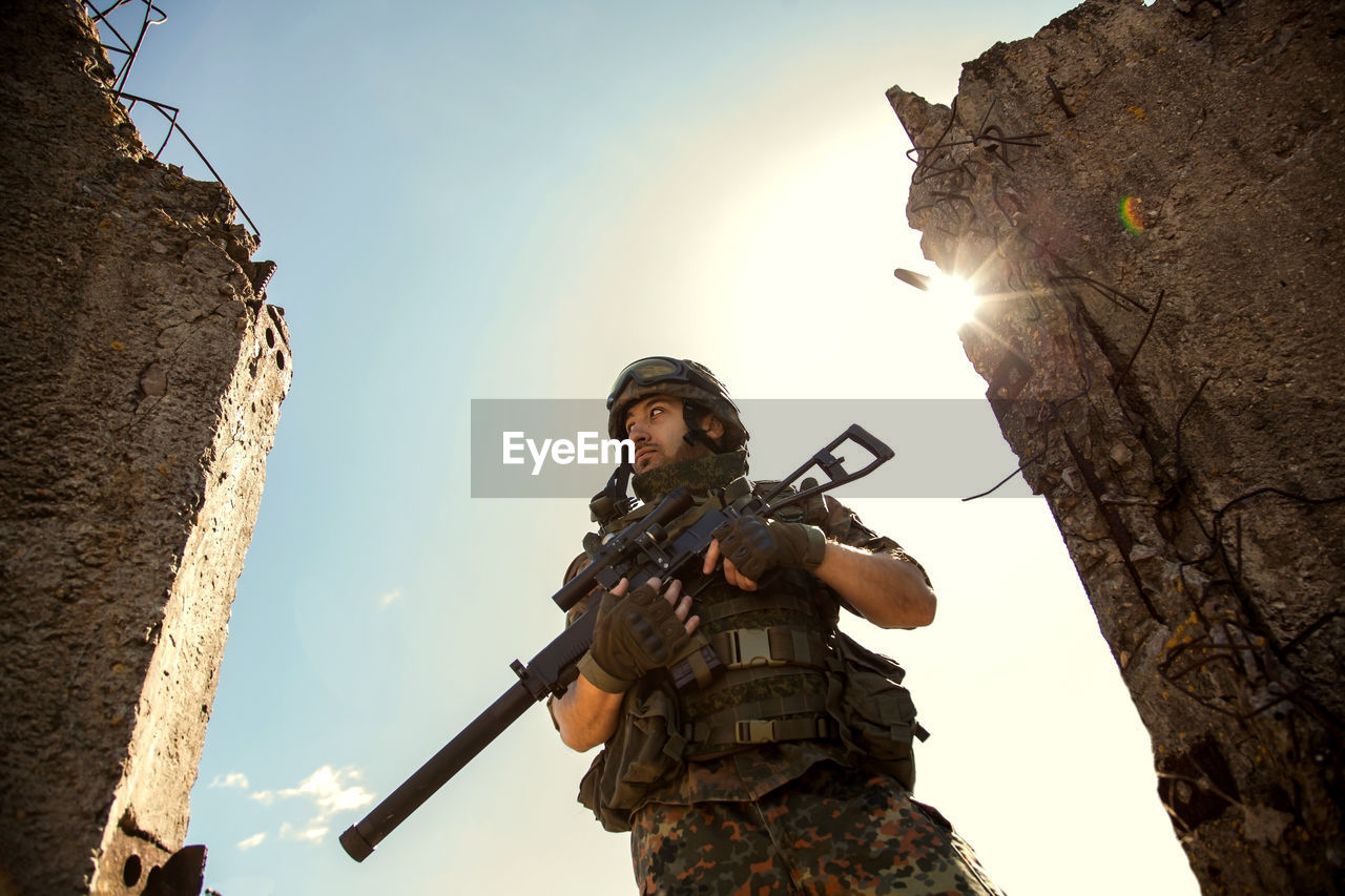 Young soldiers with guns, a soldier in equipment and with arms inspects a ruined house outside the