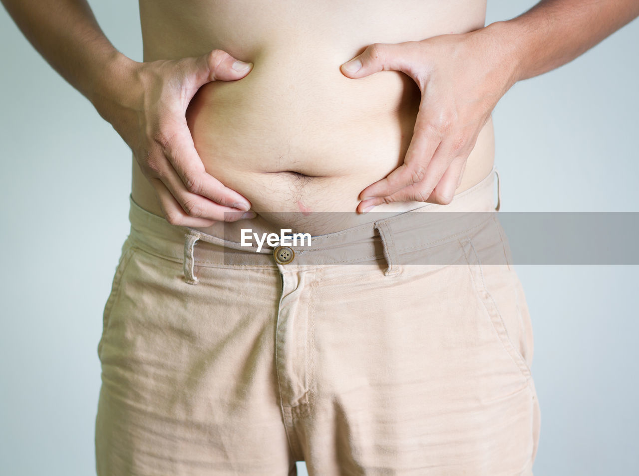 Midsection of man holding belly against gray background