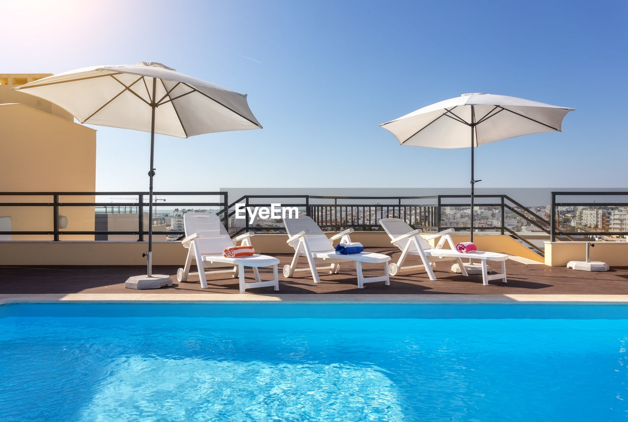 DECK CHAIRS BY SWIMMING POOL AGAINST CLEAR BLUE SKY