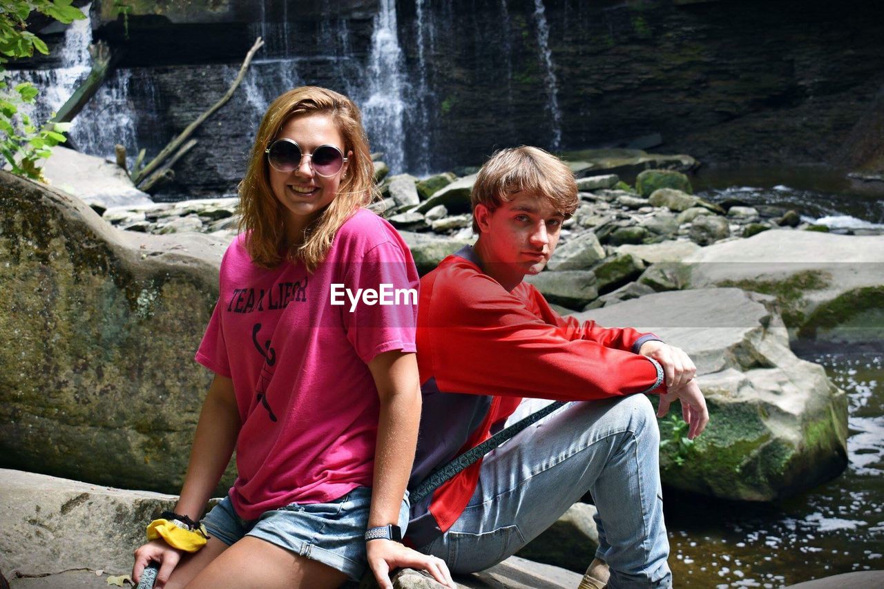 Portrait of couple sitting on rock against waterfall