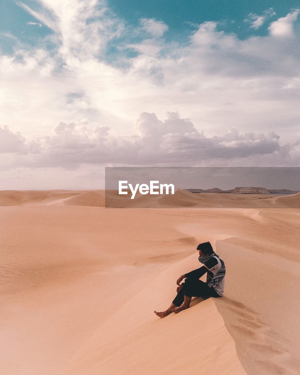 Man sitting on desert against cloudy sky