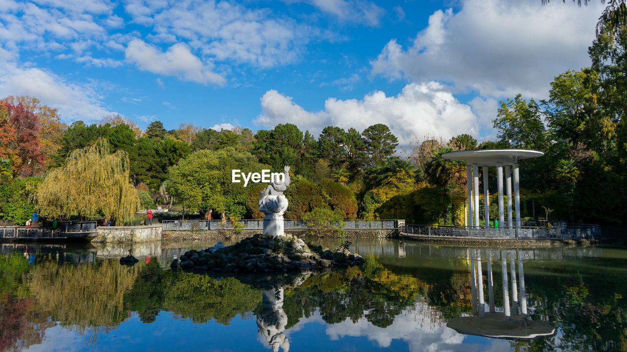 STATUE BY LAKE AGAINST TREES AND SKY
