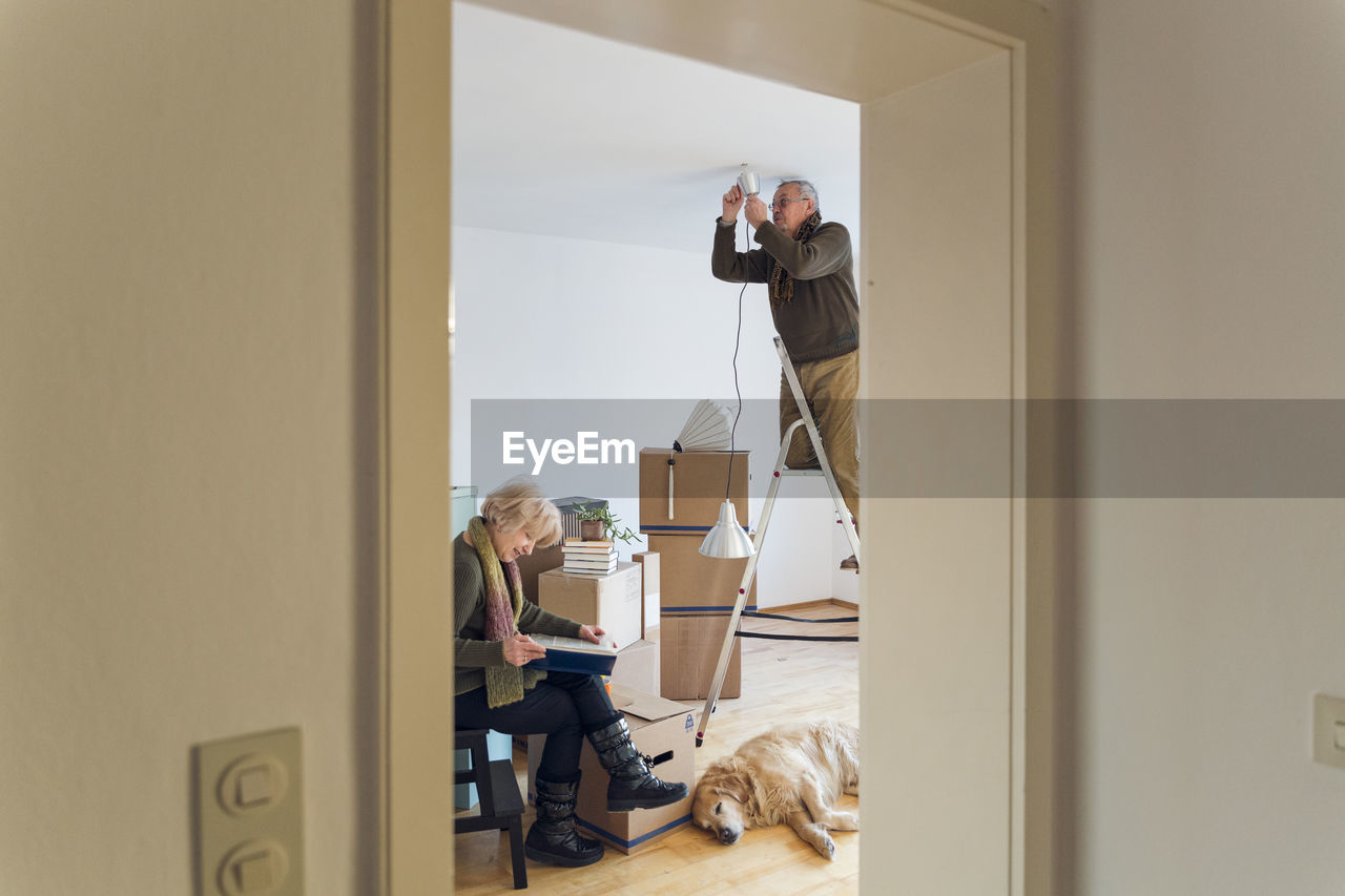 Senior couple in a new home with man mounting ceiling lamp