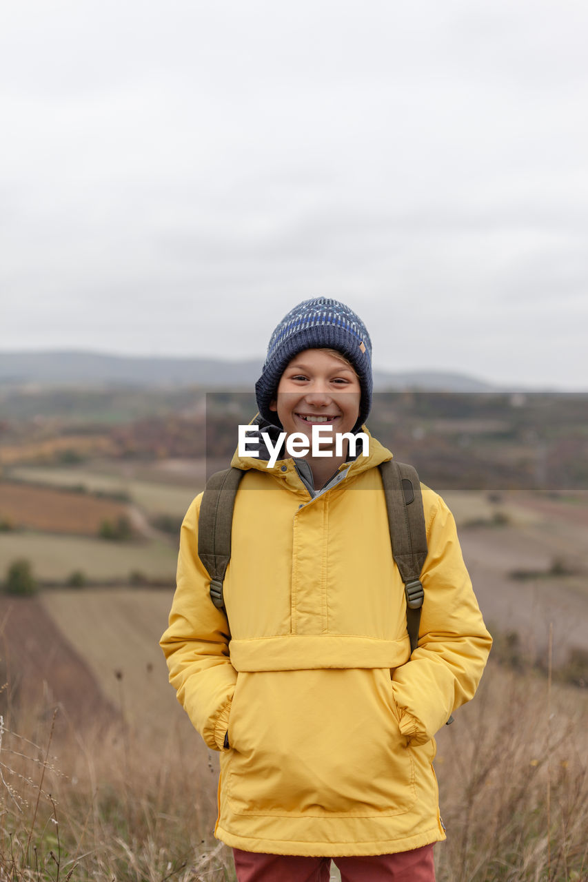 Happy elementary boy standing in nature during autumn day and looking at camera. copy space.