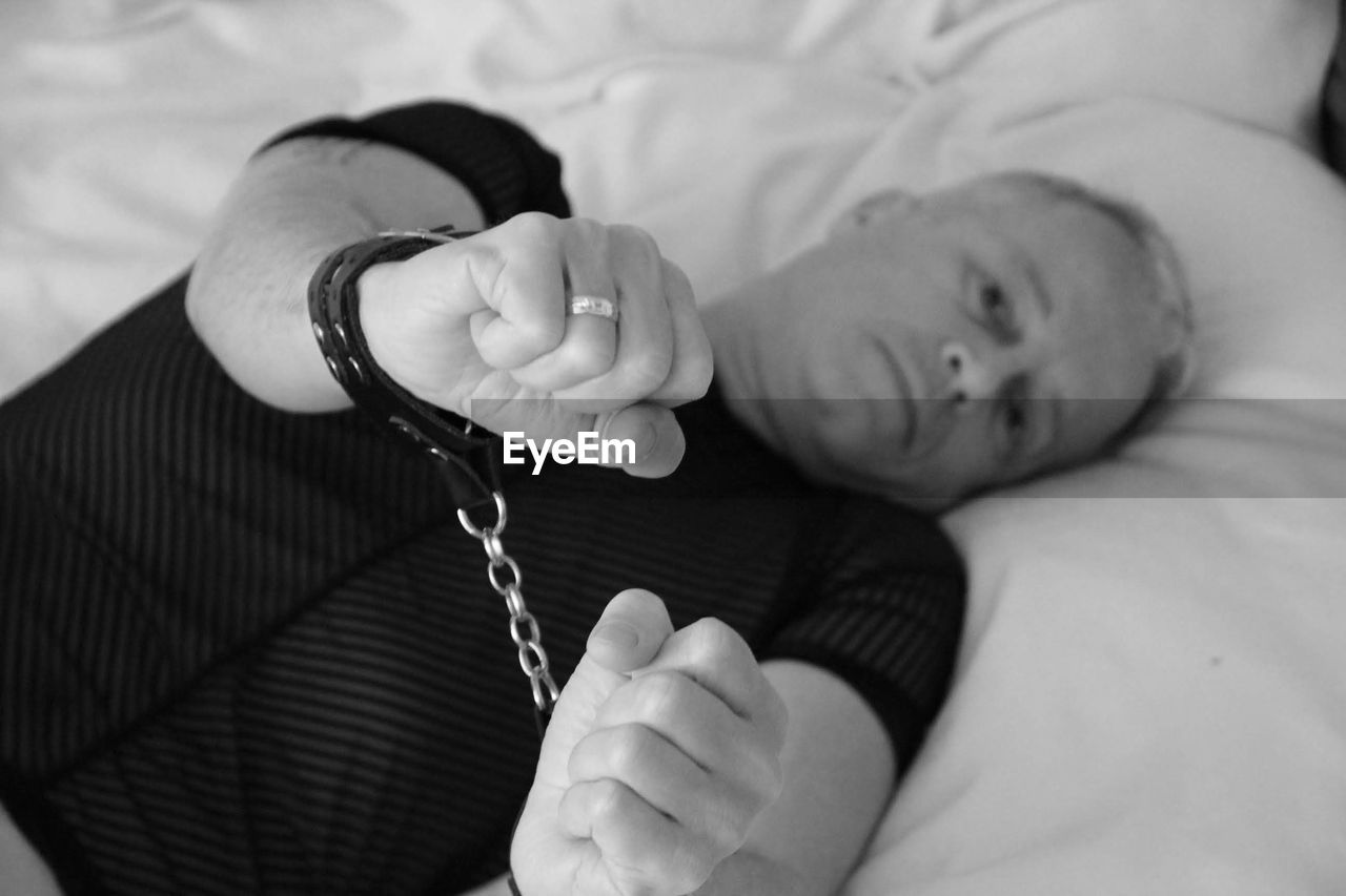Portrait of mature man wearing handcuffs lying on bed