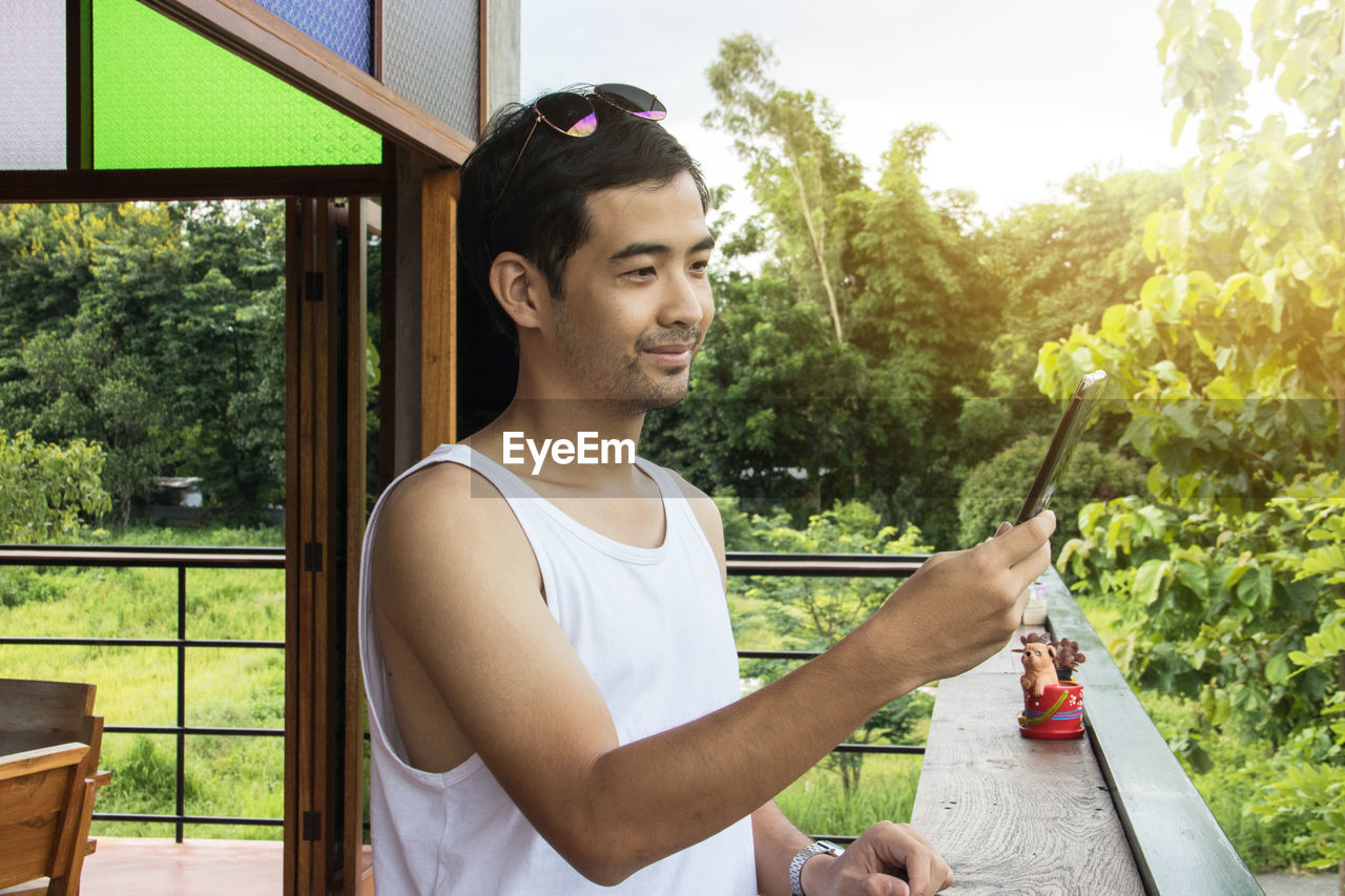 Young man using mobile phone while standing in balcony