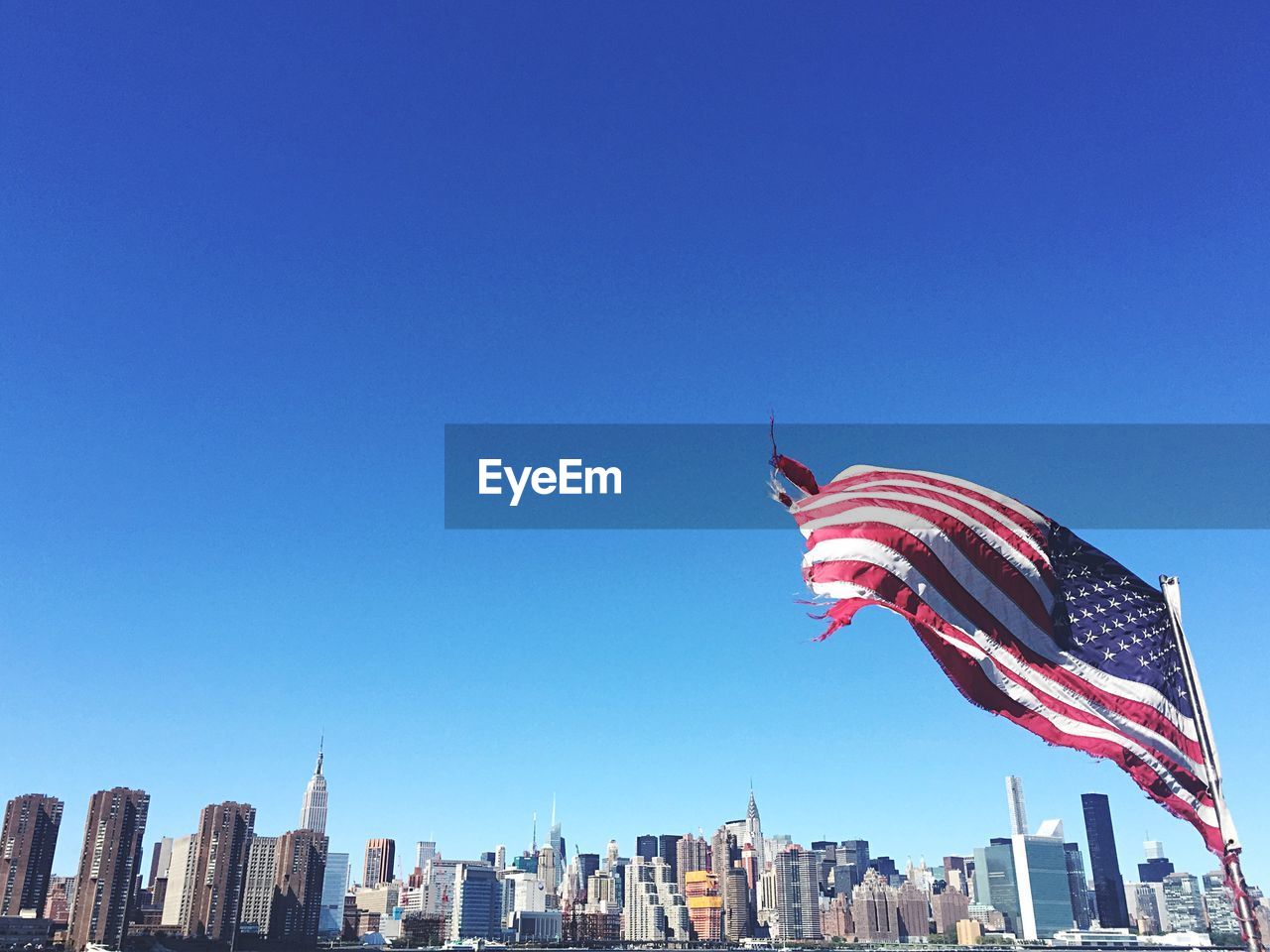 Low angle view of torn american flag blowing against clear sky in city