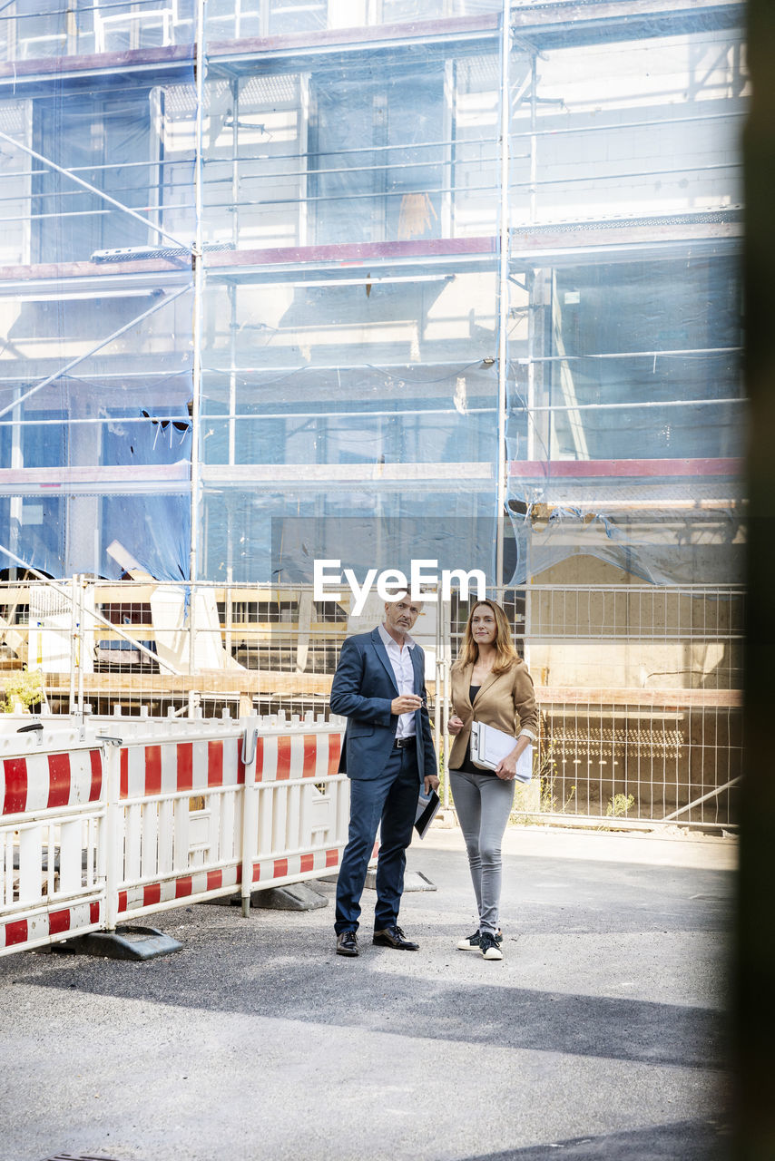 Building contractor examining construction site with businesswoman while standing against building