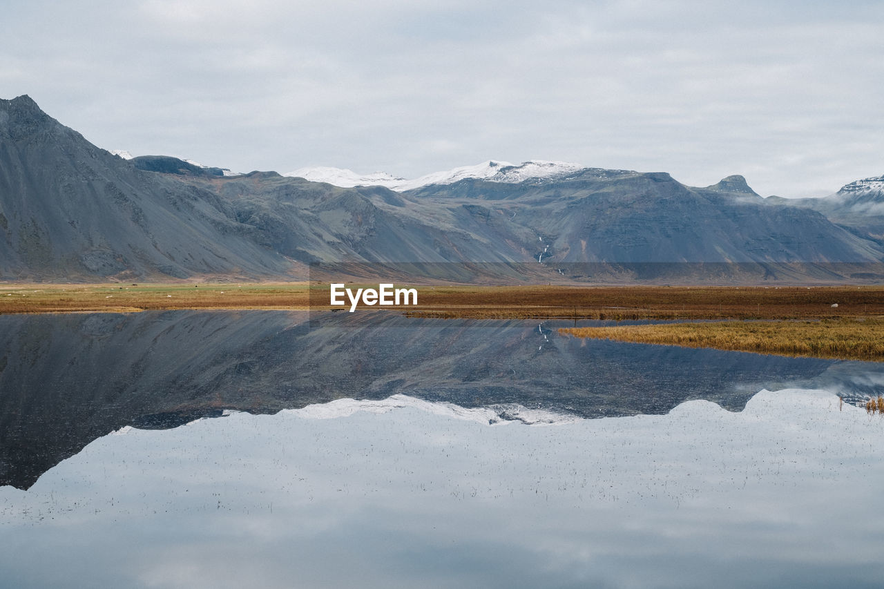 Scenic view of calm lake by mountains against cloudy sky