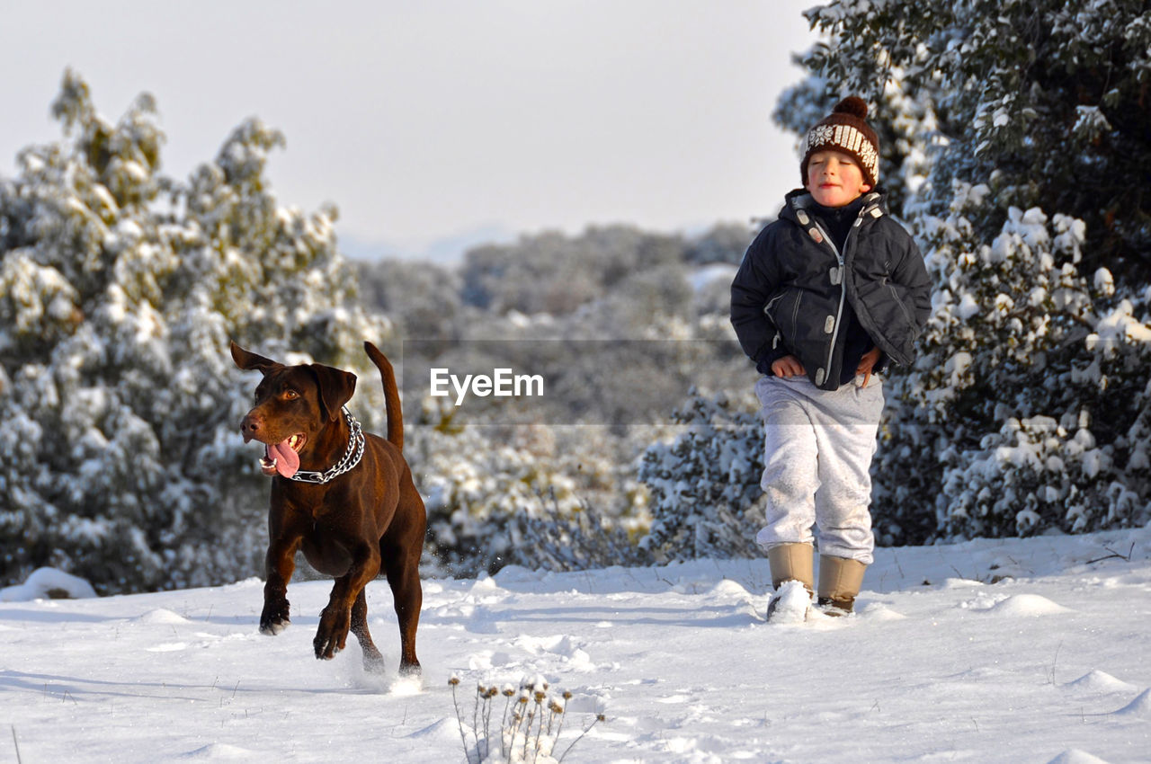 Boy walking with dog on snow covered field