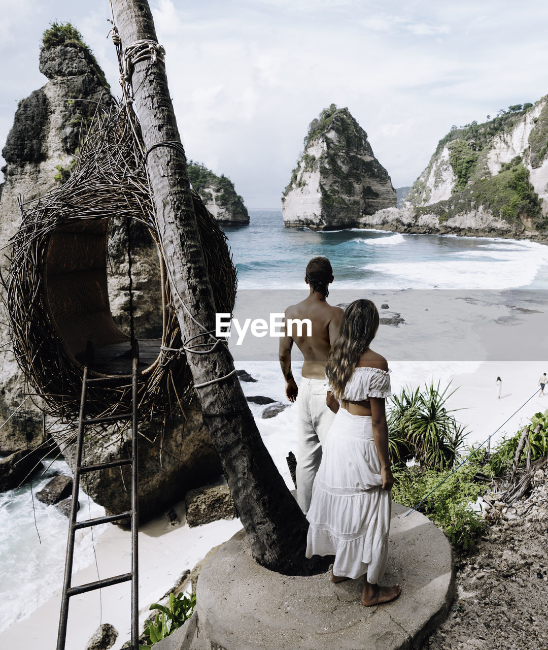 Rear view of couple standing by swing while looking at beach against sky