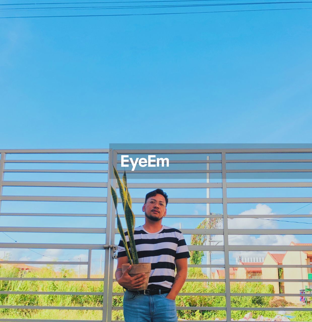 Full length of young man standing against blue sky, enjoying a beautiful day. 