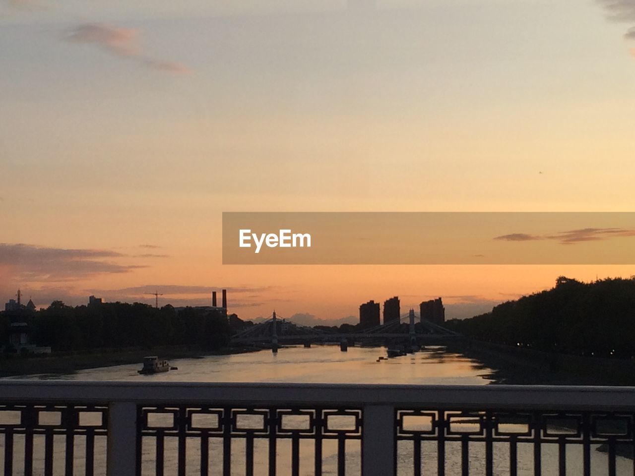 Bridge over river in city against sky at sunset