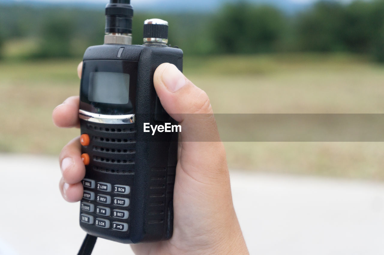 Close-up of hand holding walkie-talkie against sky