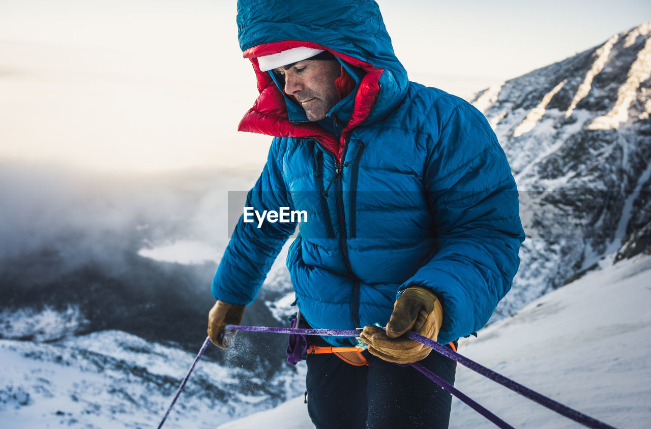 Male climber belays his lead climber during a cold winter alpine climb