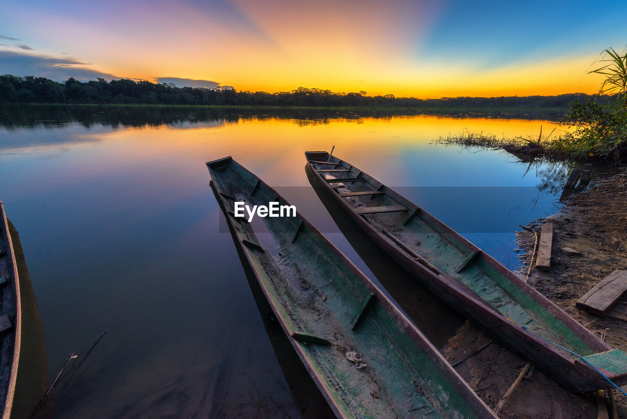 Wooden canoes moored on lake against sky during sunset