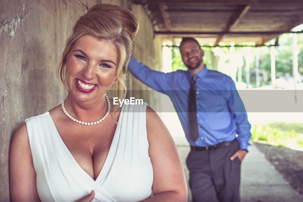 Portrait of bride smiling while groom leaning on wall