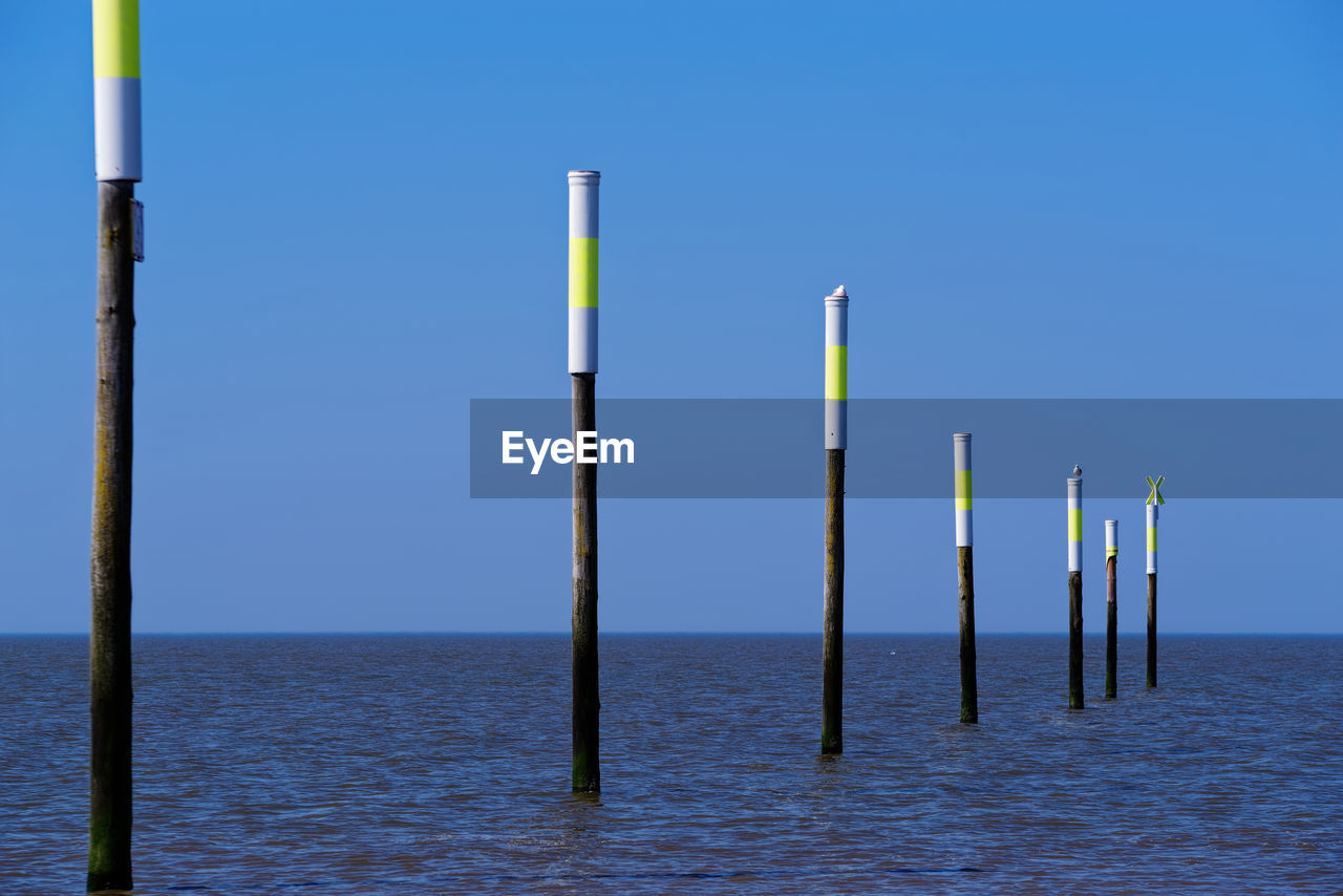 Wooden posts in sea against clear blue sky