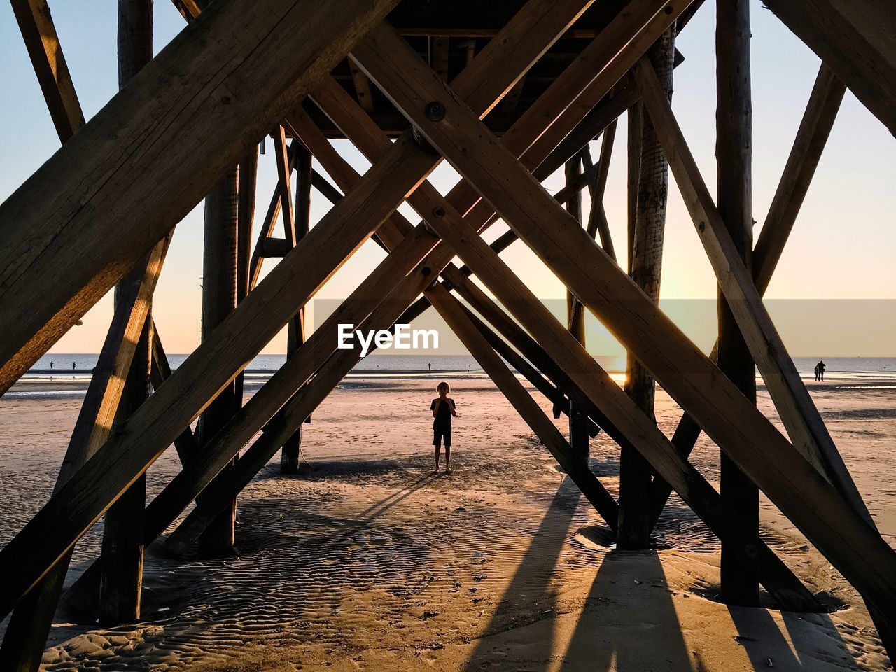 Rear view of man standing on pier at beach against sky