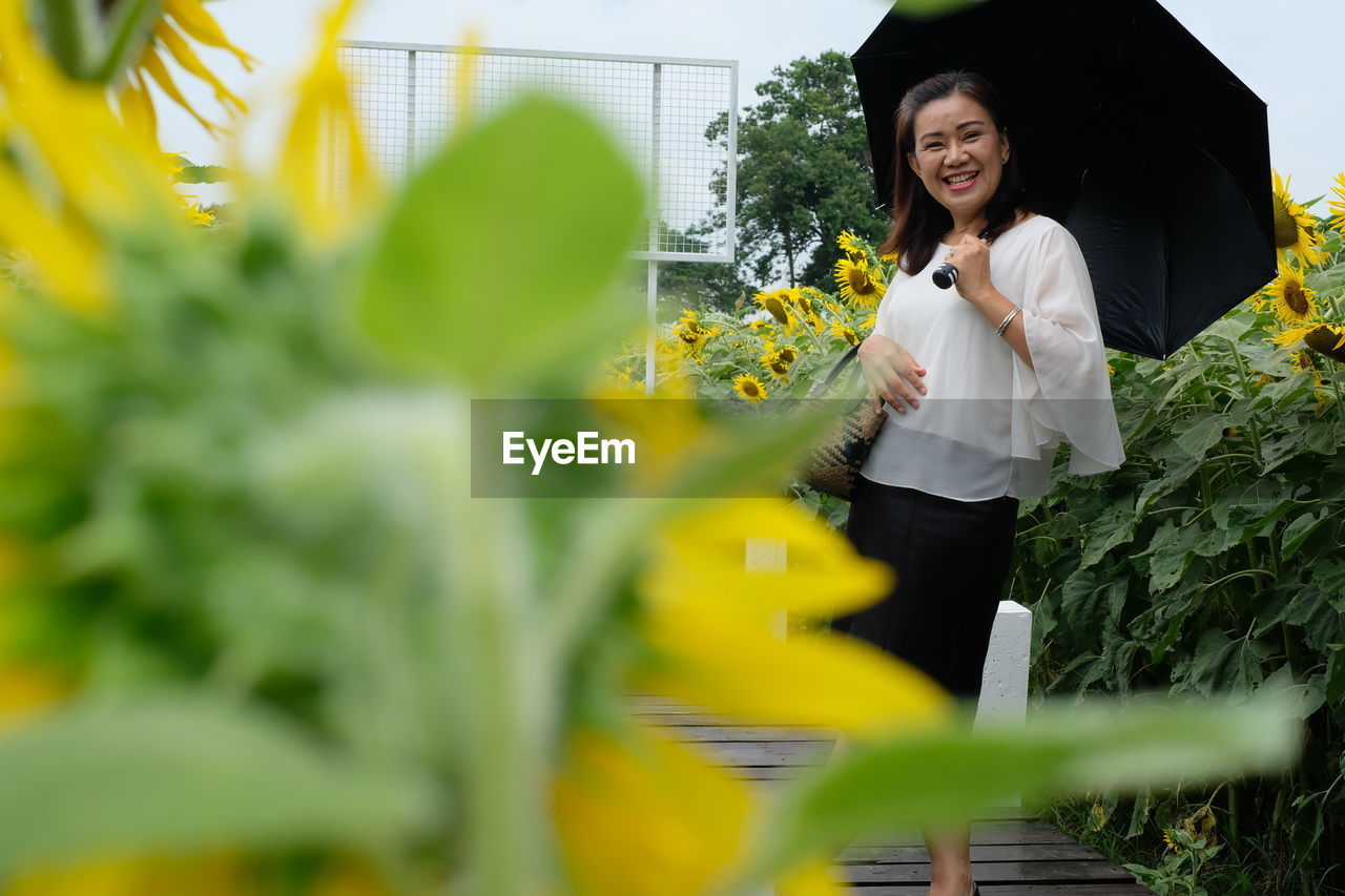 Portrait of smiling woman with umbrella while standing on sunflower field