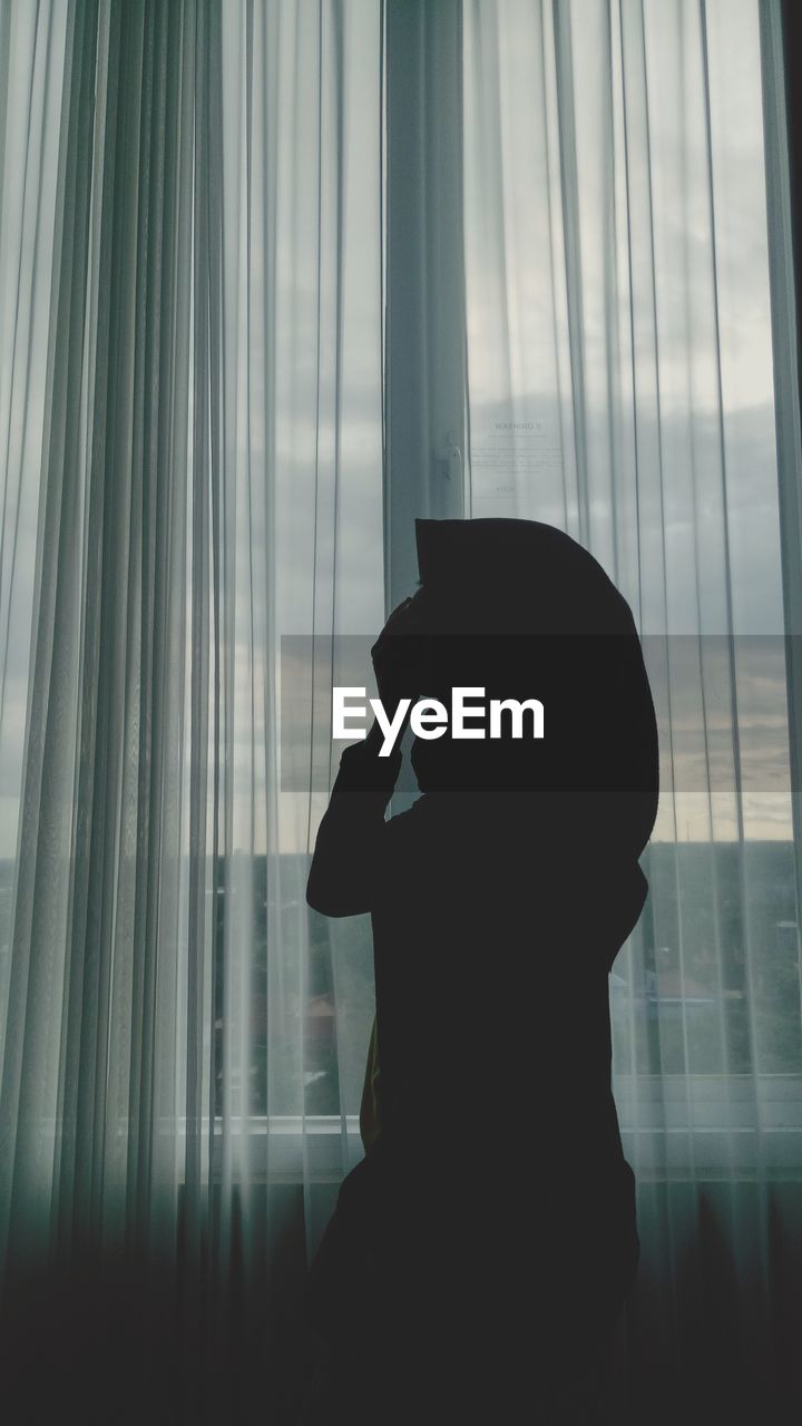 Silhouette woman standing by curtain