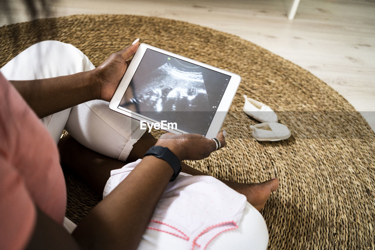 Pregnant woman holding digital tablet with ultrasound video at home