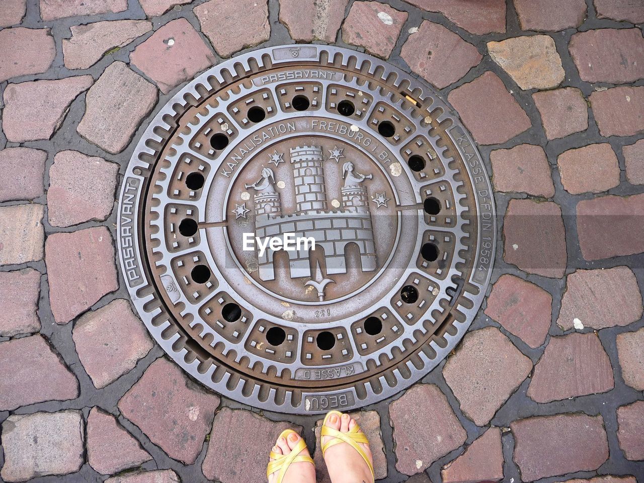 Low section of woman standing in front of manhole