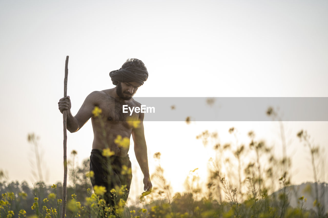Young indian farmer with a stick walking in a wasteland. crops not growing due to shortage