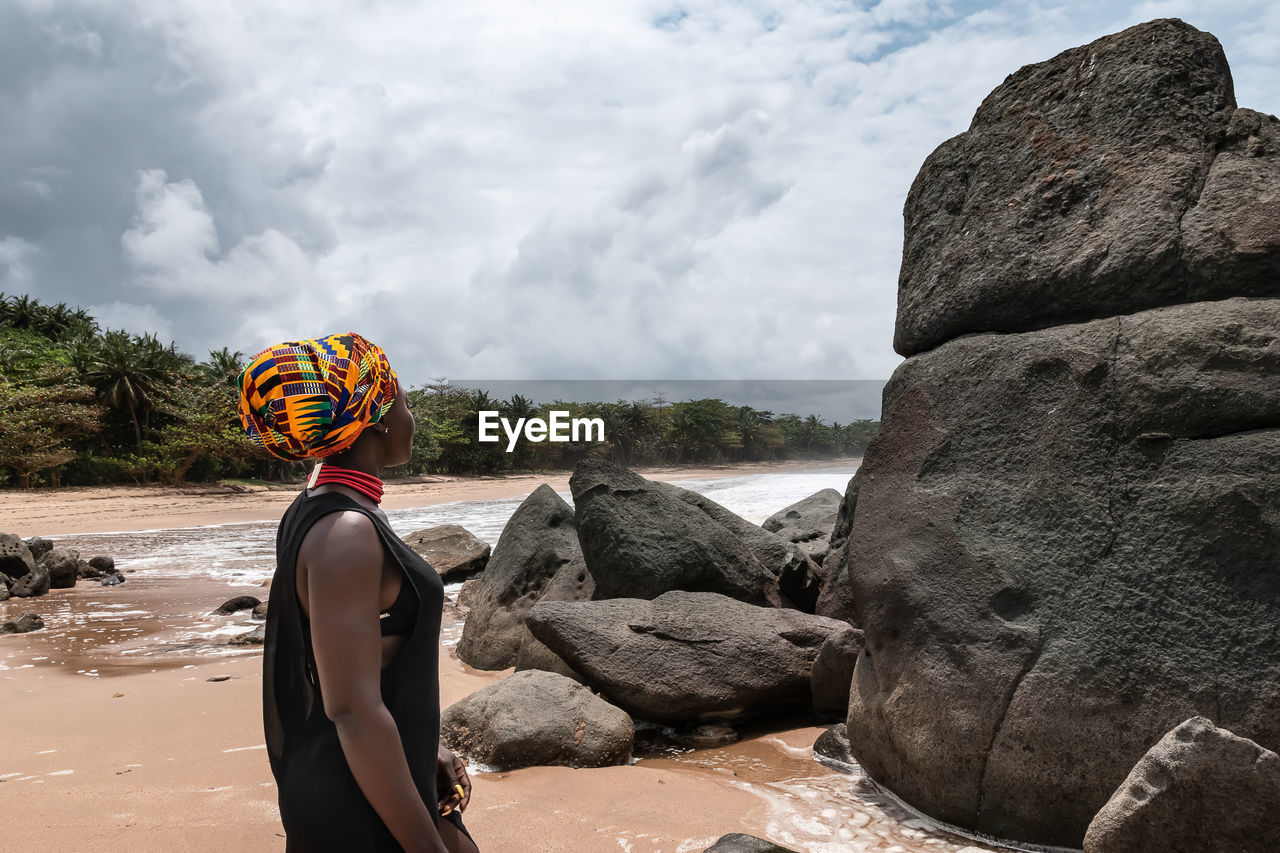 African woman standing on a beautiful beach with dark big stones