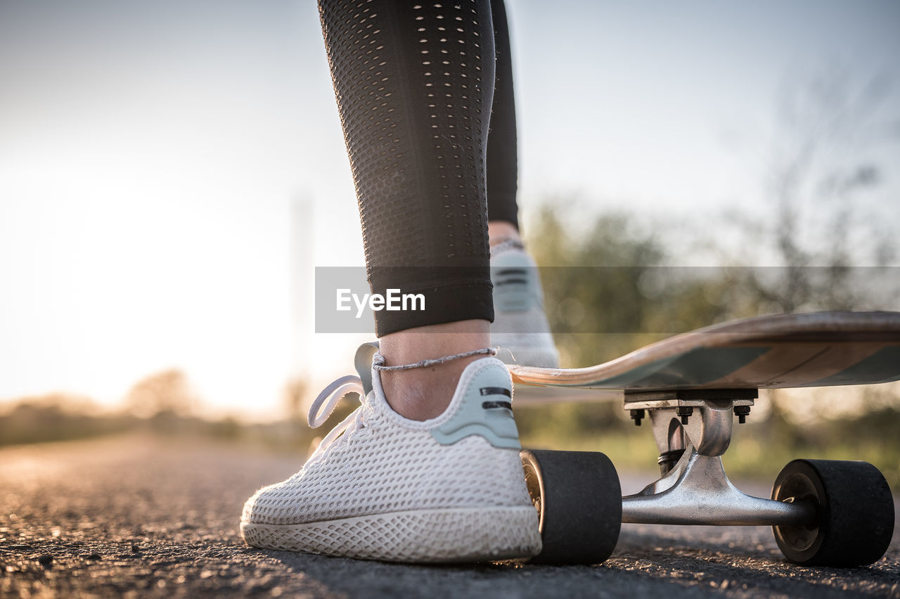 Low section of woman skateboarding on road