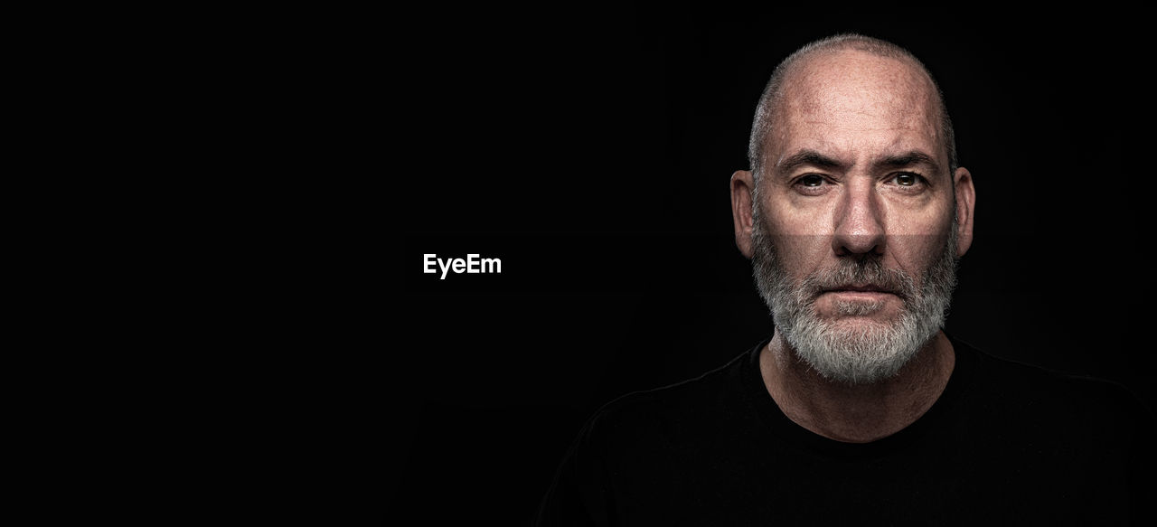 portrait of serious man standing against black background