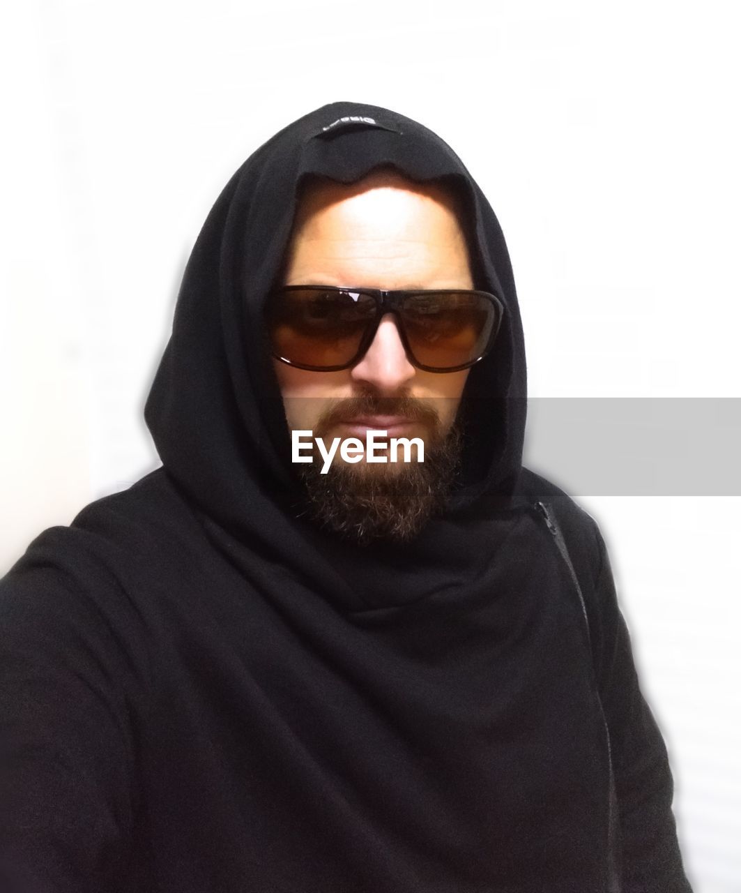 one person, portrait, fashion, adult, hood, beard, men, facial hair, sunglasses, hood - clothing, clothing, glasses, hooded shirt, hoodie, black, young adult, headscarf, cool attitude, headshot, studio shot, white background, looking at camera, front view, outerwear, person, indoors, cut out, serious, lifestyles, hijab, casual clothing, copy space, emotion, human face, waist up