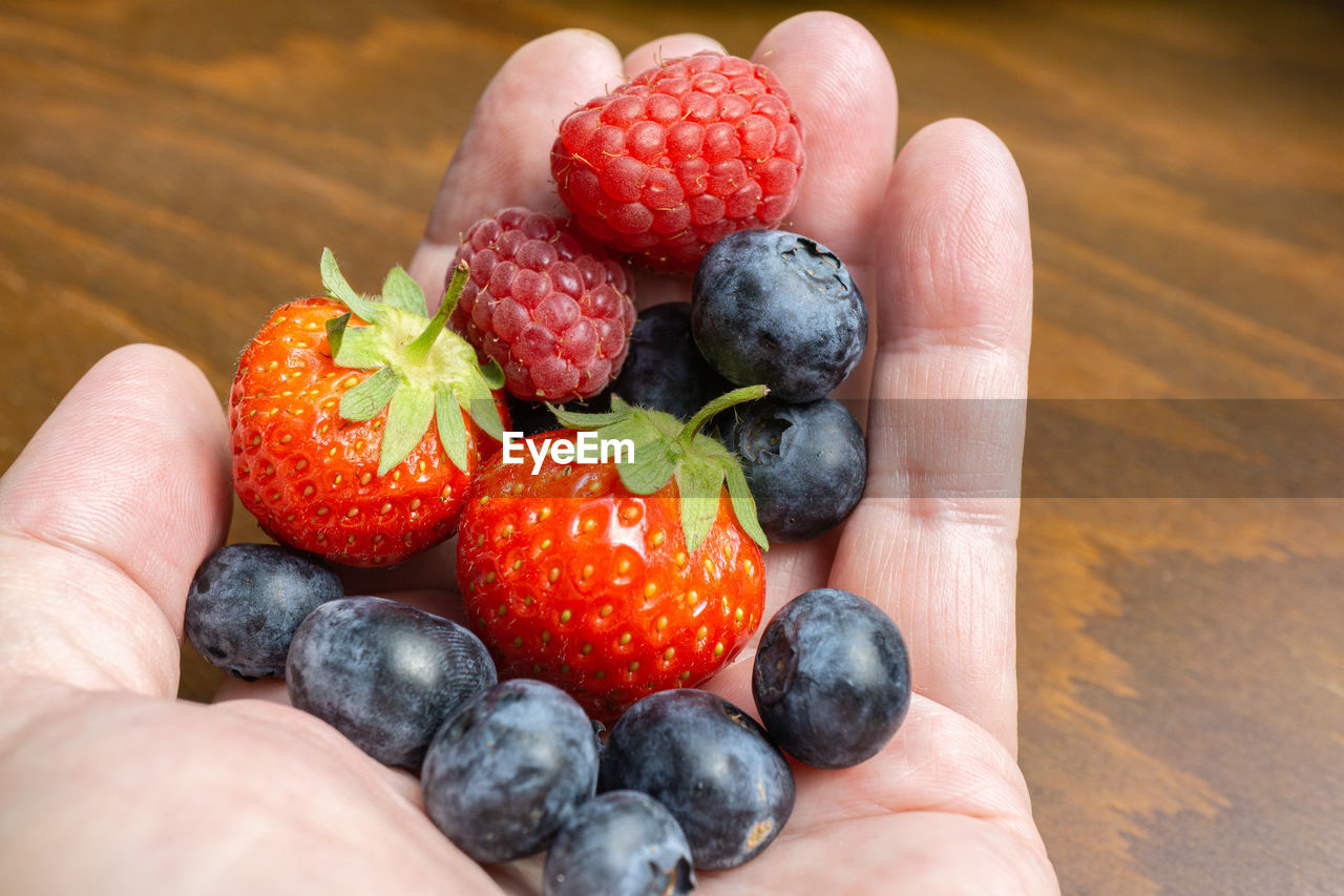 Hand with fruits, strawberries, raspberries and blueberries
