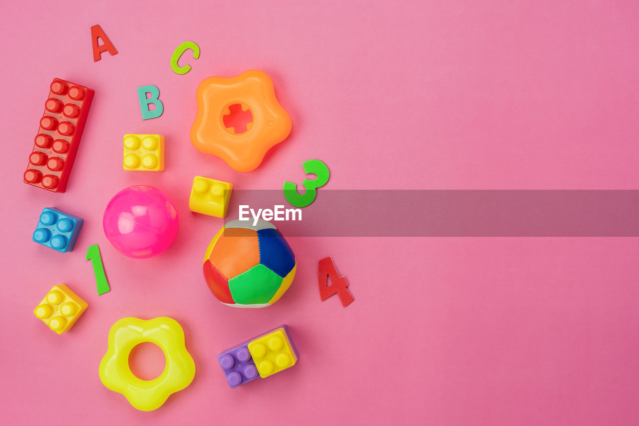 HIGH ANGLE VIEW OF MULTI COLORED TOYS ON PINK BACKGROUND